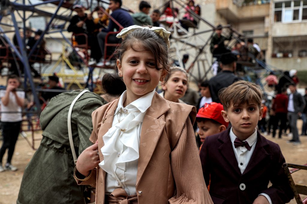 SÍRIA: Crianças vestidas com roupas novas posam para uma foto ao lado de um parquinho no primeiro dia do feriado muçulmano do Eid Al-Fitr.
