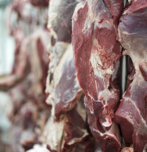 Fresh red meet and butchery worker working in background.