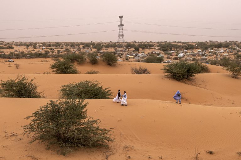 Three men look for a place to sit for the evening along a dune in Nouakchott, Mauritania, on June 30, 2024. (Photo by JOHN WESSELS / AFP)