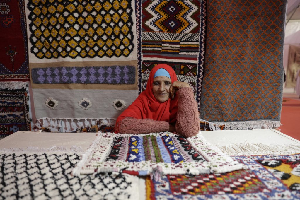 An Amazigh woman displays carpets that she wove, during the seventh edition of the annual Ouaouzguit Carpet Festival, in the town of Tazenakht in MOrocco's Ouarzazat province on November 21, 2024. - In southern Morocco, women are the guardians of the age-old craft of carpet weaving, an intricate art form practiced on small traditional looms where a single carpet can take two to four weeks to make depending on size. But this vital source of income often leaves them with meagre earnings, making it less attractive for younger women, putting this heritage at risk of disappearing. (Photo by AFP)