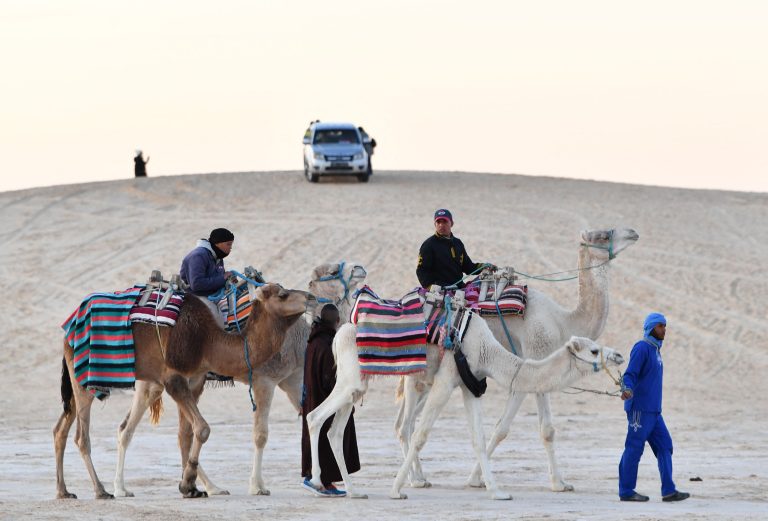 Tunisian men walk with their camels on December 26, 2023 in Nafta, near Tozeur, in the Sahara desert in south-western Tunisia. (Photo by FETHI BELAID / AFP)