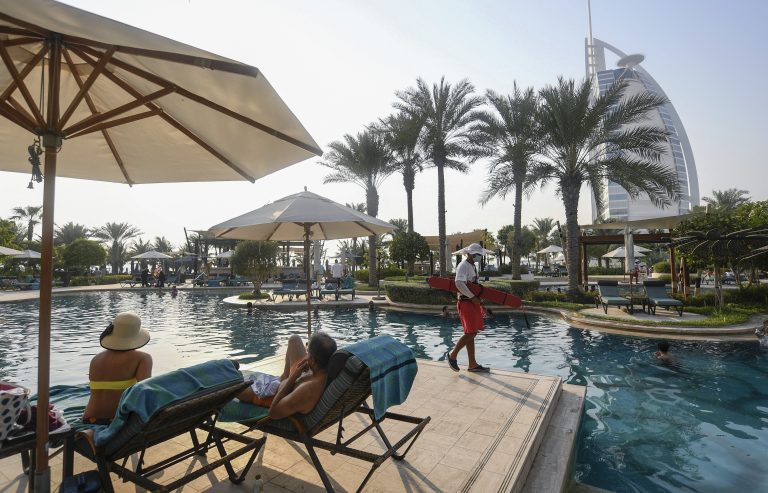 Tourists sunbathe by the pool of the Al Naseem hotel in the Gulf emirate of Dubai in the United Arab Emirates, on July 7, 2020, with a view of the Burj al-Arab hotel in the background. With a "welcome" passport sticker and coronavirus tests on arrival, Dubai reopens its doors to international visitors in the hope of reviving its tourism industry after a nearly four-month closure. (Photo by KARIM SAHIB / AFP)